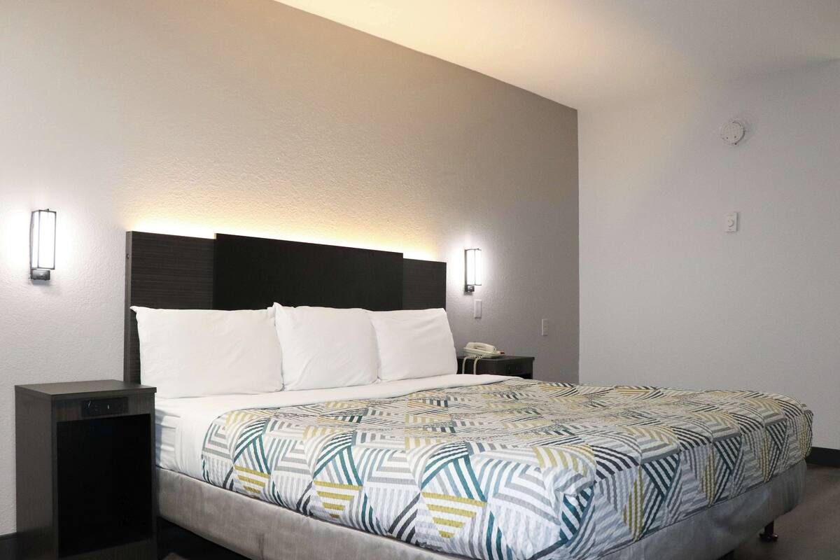A hotel room with a bed, bedside tables, and wall-mounted lights.