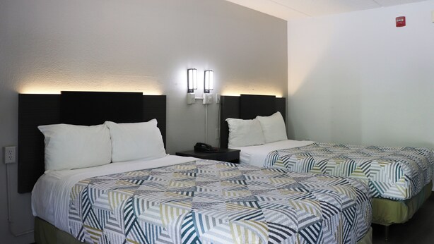 A hotel room with two beds, each with a patterned bedspread and white pillows. There are bedside tables with lamps and a red emergency exit sign on the wall. - Motel 6 Birmingham, AL (Birmingham)