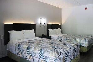 A hotel room with two beds, each with a patterned bedspread and white pillows. There are bedside tables with lamps and a red emergency exit sign on the wall. - Motel 6 Birmingham, AL (Birmingham)