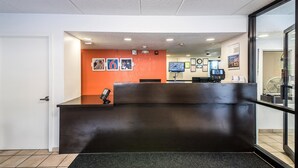 A reception area with a dark reception desk, a clock, and a television screen. - Motel 6 Birmingham, AL (Birmingham)