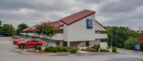 A motel with a red roof and a blue sign indicating it is a 6-star establishment. There are several cars parked in the lot.