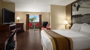 A hotel room with a bed, a television, a fireplace, a balcony with red chairs, and a Canadian flag. - Super 8 by Wyndham Brockville (Elizabethtown-Kitley)