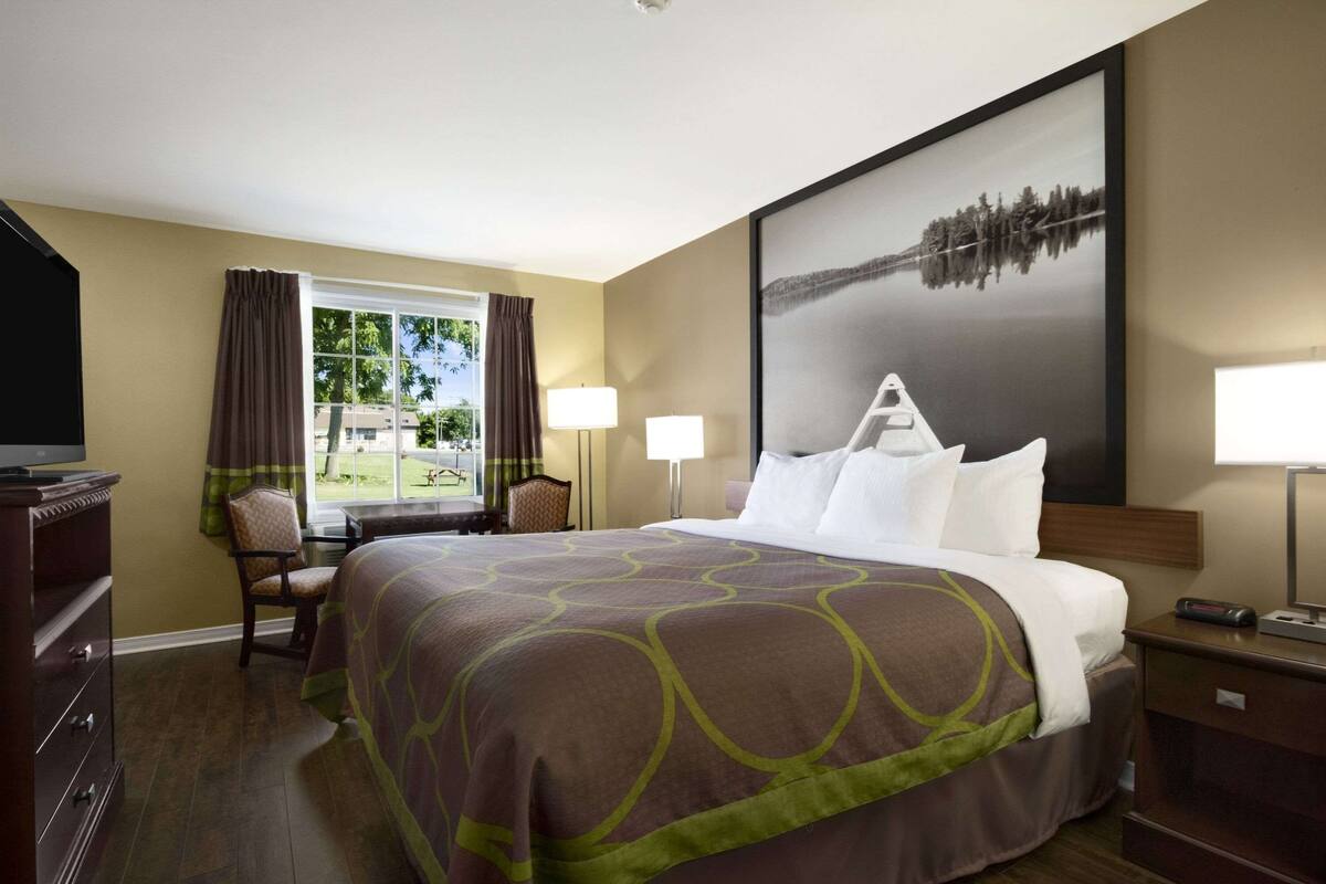 Una habitación de hotel con una cama grande, un escritorio, una silla, un televisor y una ventana con cortinas.