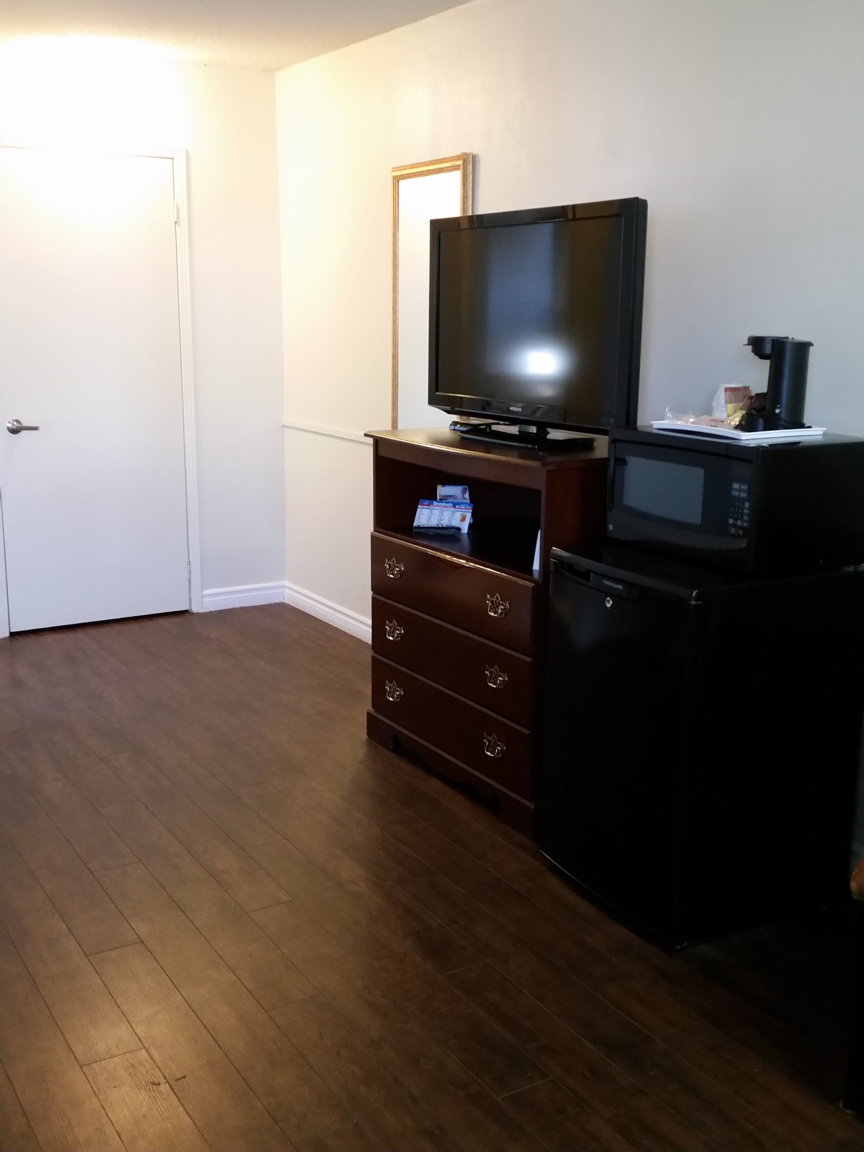 A room with a wooden floor, a television on a wooden stand, a microwave, and a small cabinet with drawers.