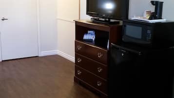 A room with a wooden floor, a television on a wooden stand, a microwave, and a small cabinet with drawers.