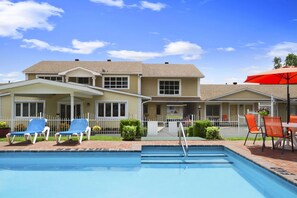 A pool area with lounge chairs and a red umbrella.
