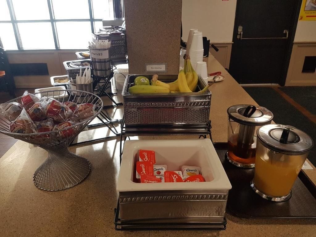 A buffet setup with food items, a fruit basket, and a beverage dispenser.