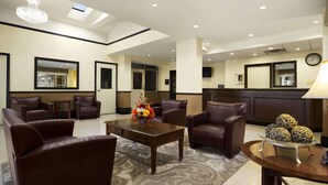 A hotel lobby with leather chairs, a wooden coffee table with a floral centerpiece, and a reception desk. - Super 8 by Wyndham Brockville (Elizabethtown-Kitley)