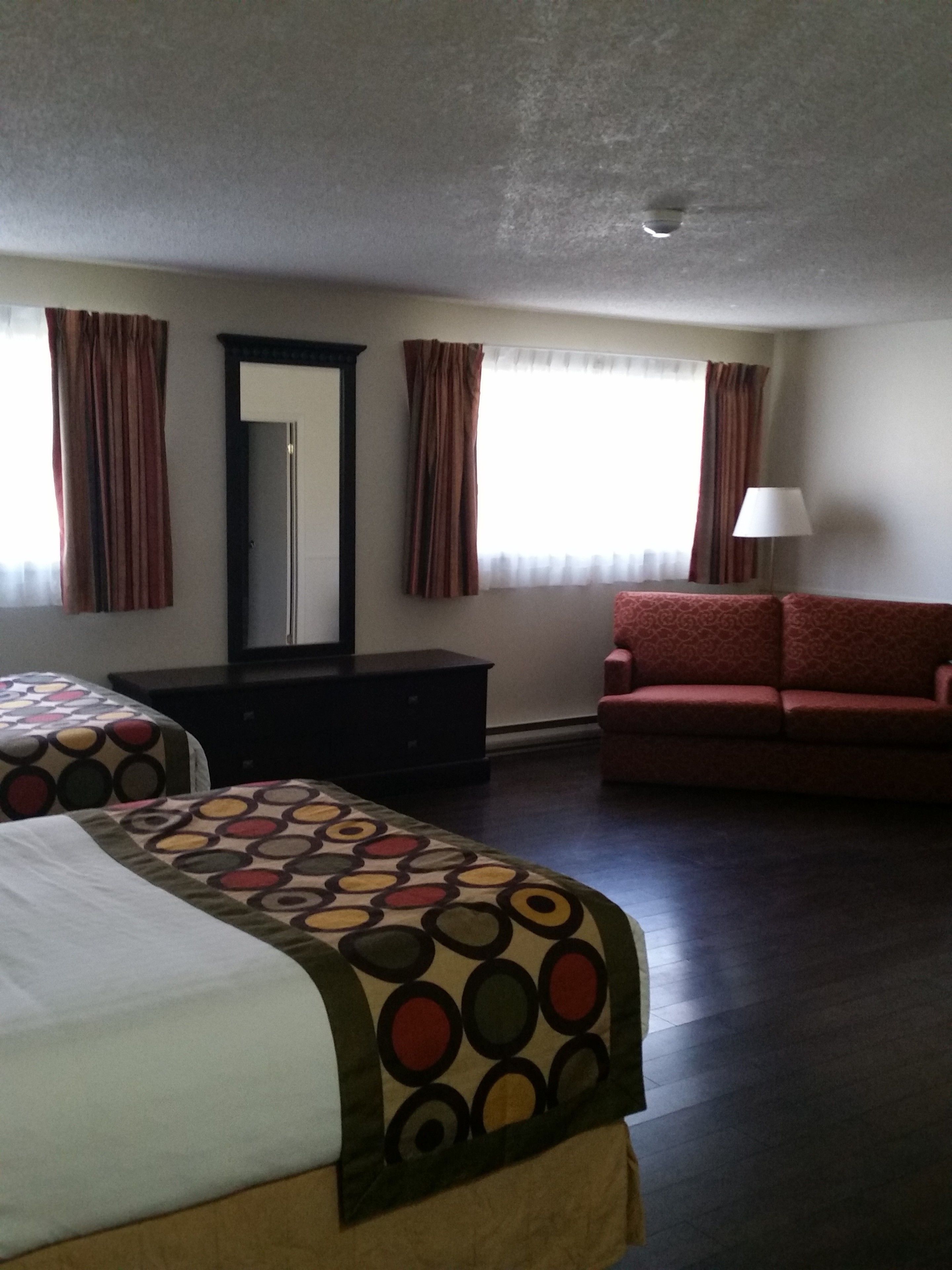 A hotel room with two beds, a sofa, a dresser, and a mirror.