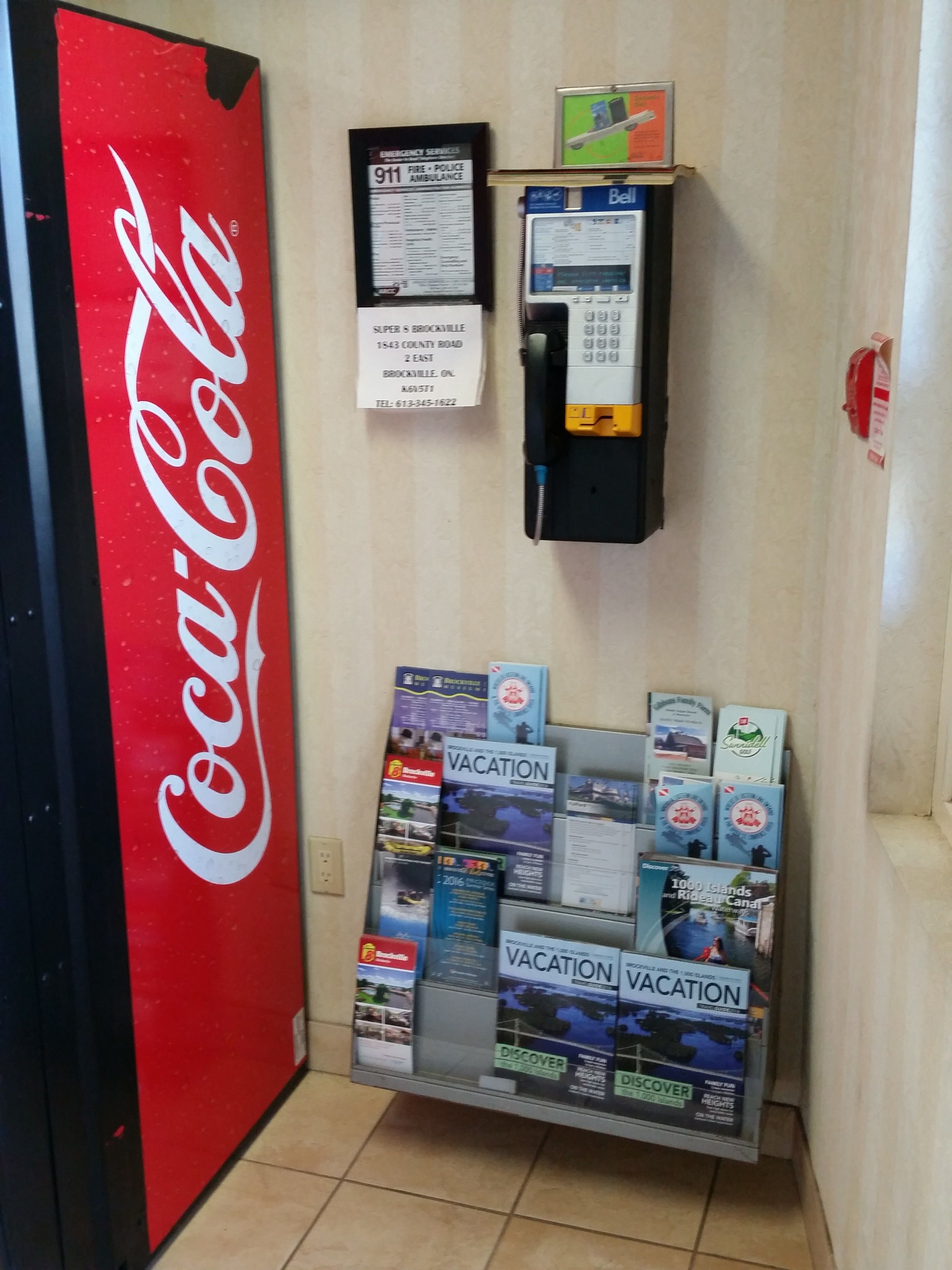 Un distributeur automatique de Coca-Cola, un panneau indiquant les services d’urgence et un présentoir rempli de brochures de voyage.
