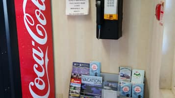 Un distributeur automatique de Coca-Cola, un panneau indiquant les services d’urgence et un présentoir rempli de brochures de voyage.