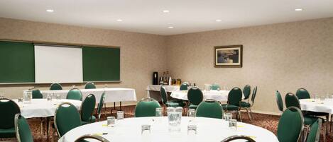 A conference room with round tables, green chairs, white tablecloths, and a projector screen.