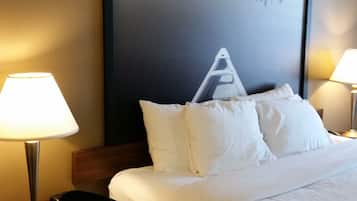 Quarto de hotel com cama, duas luminárias de cabeceira, uma cadeira e um quadro grande na parede.