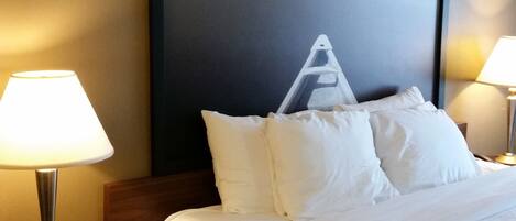 Una habitación de hotel con una cama, dos lámparas de noche, una silla y un cuadro grande enmarcado en la pared.