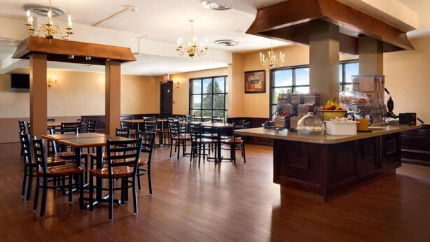 A spacious dining area with wooden tables and chairs, a central island with food and drinks, and large windows providing natural light. - Super 8 by Wyndham Brockville (Elizabethtown-Kitley)