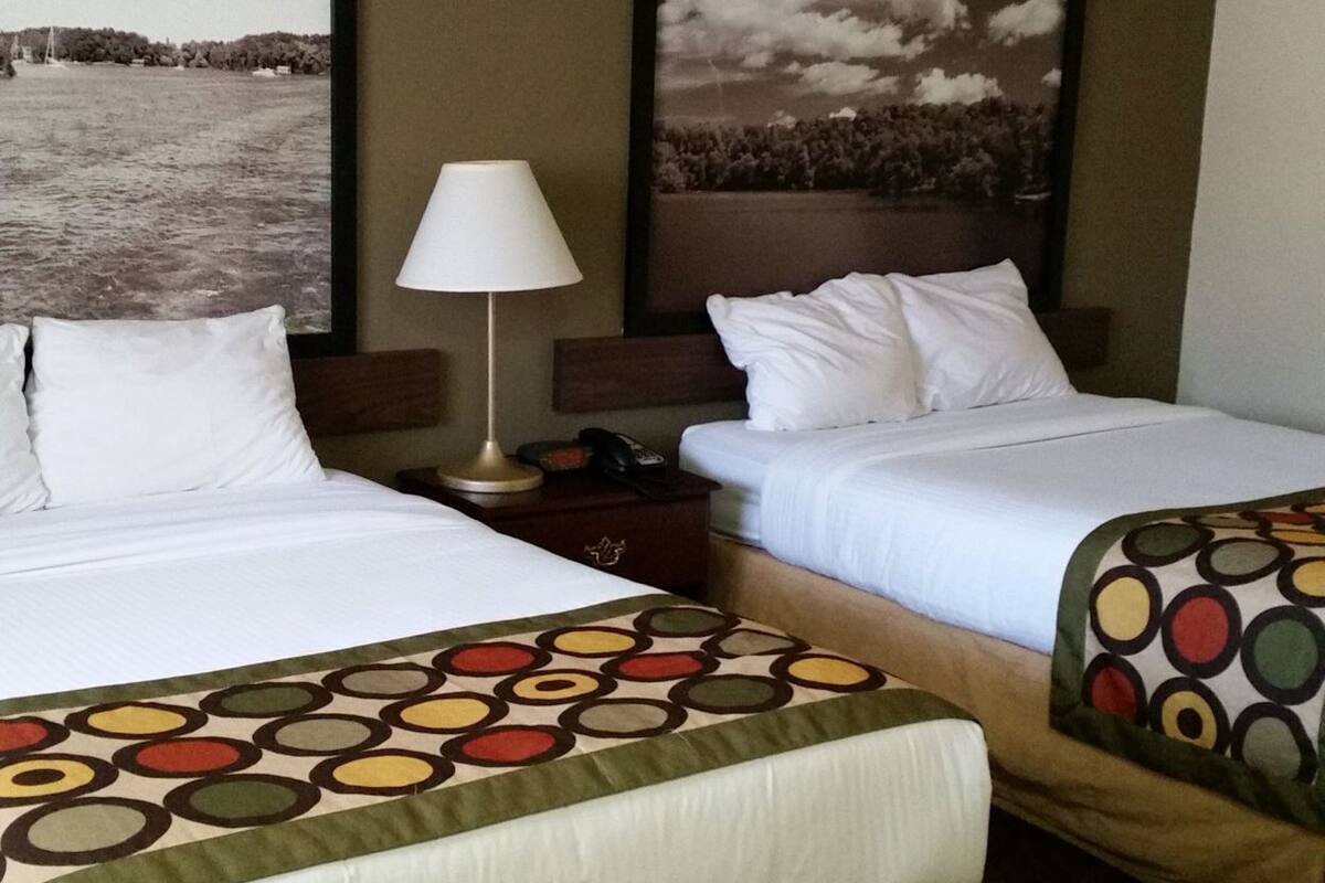 Habitación de hotel con dos camas, una mesita de noche, una lámpara y dos grandes cuadros con paisajes en las paredes.