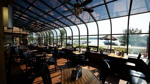 A restaurant with a curved glass roof, tables, chairs, and a view of the outside. - Fourwinds Lakeside Inn & Marina (Bloomington)