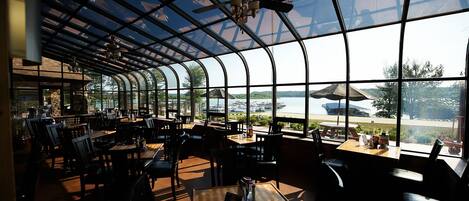 A restaurant with a curved glass roof, tables, chairs, and a view of the outside.