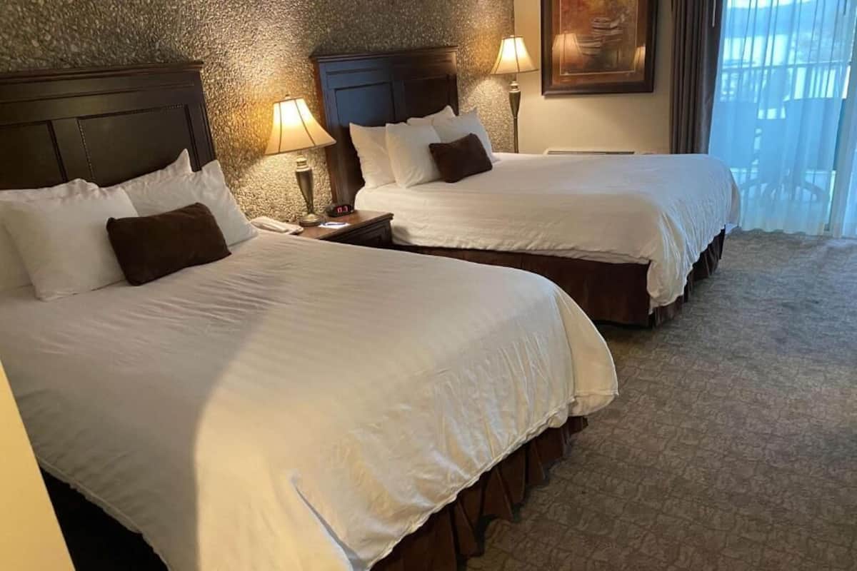 Two double beds with white linens and brown headboards in a hotel room.