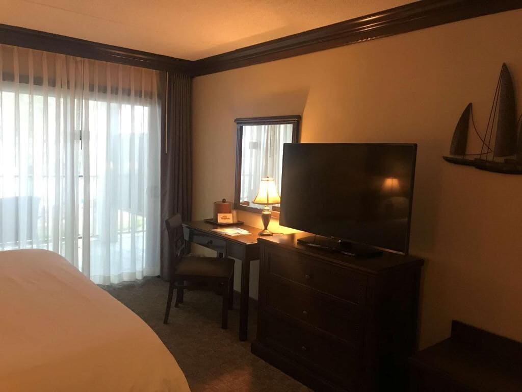 Una habitación de hotel con cama, escritorio con lámpara, televisión y ventana con cortinas.