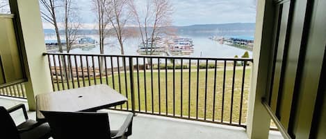 A covered balcony with a table and chairs, overlooking a marina with boats and a lake.