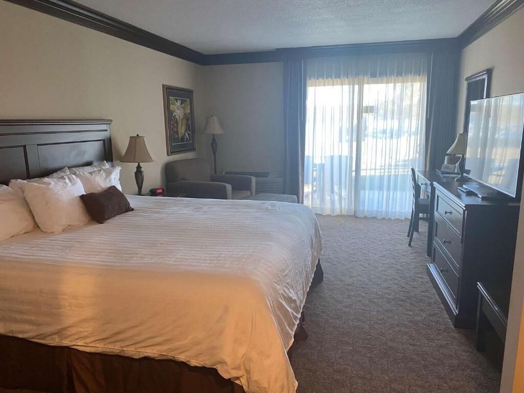 A hotel room with a large bed, a desk with a chair, a television, and a window with curtains.