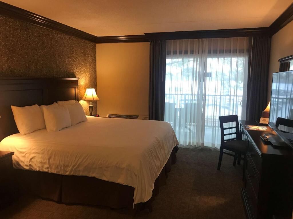 A hotel room with a large bed, a desk with a chair, a television, and a window with curtains.