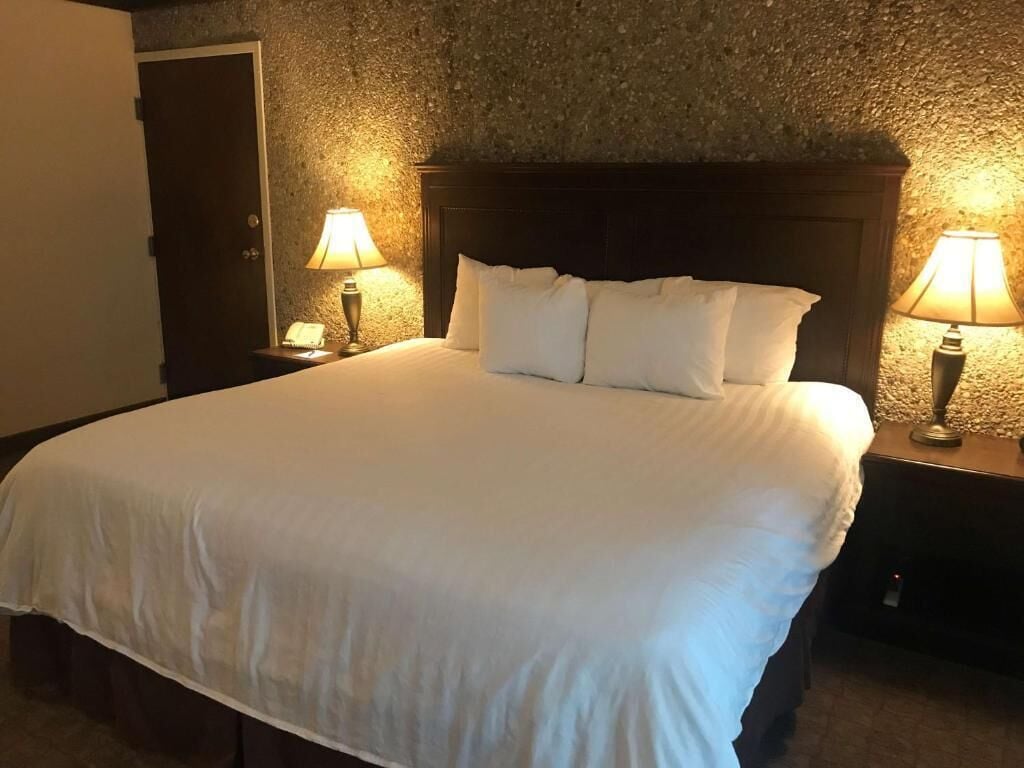 A neatly made bed with white linens, two bedside lamps, and a textured stone wall.