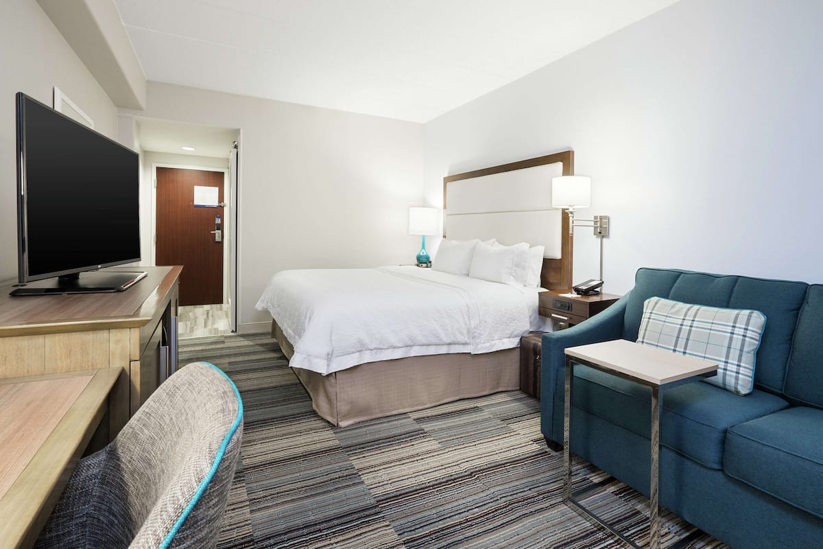 A hotel room with a bed, a TV, a desk, a chair, a sofa, and a small table.