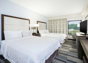 A hotel room with two beds, a desk, a television, and a window with a city view.