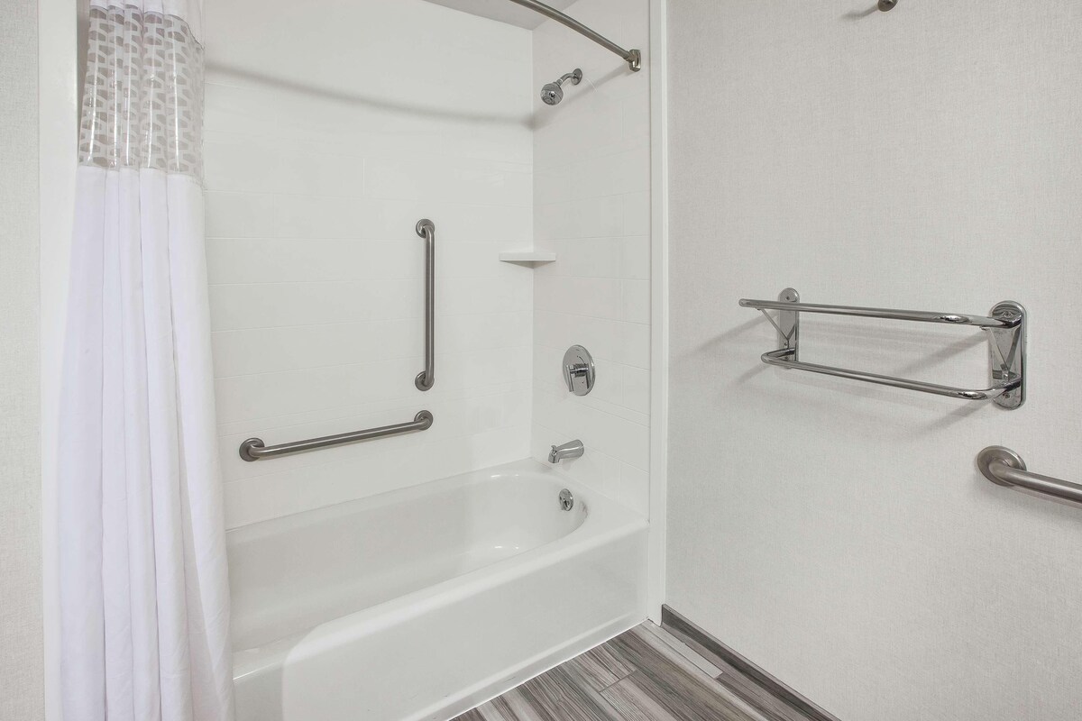 A bathroom with a bathtub, grab bars, a shower area, and a toilet.