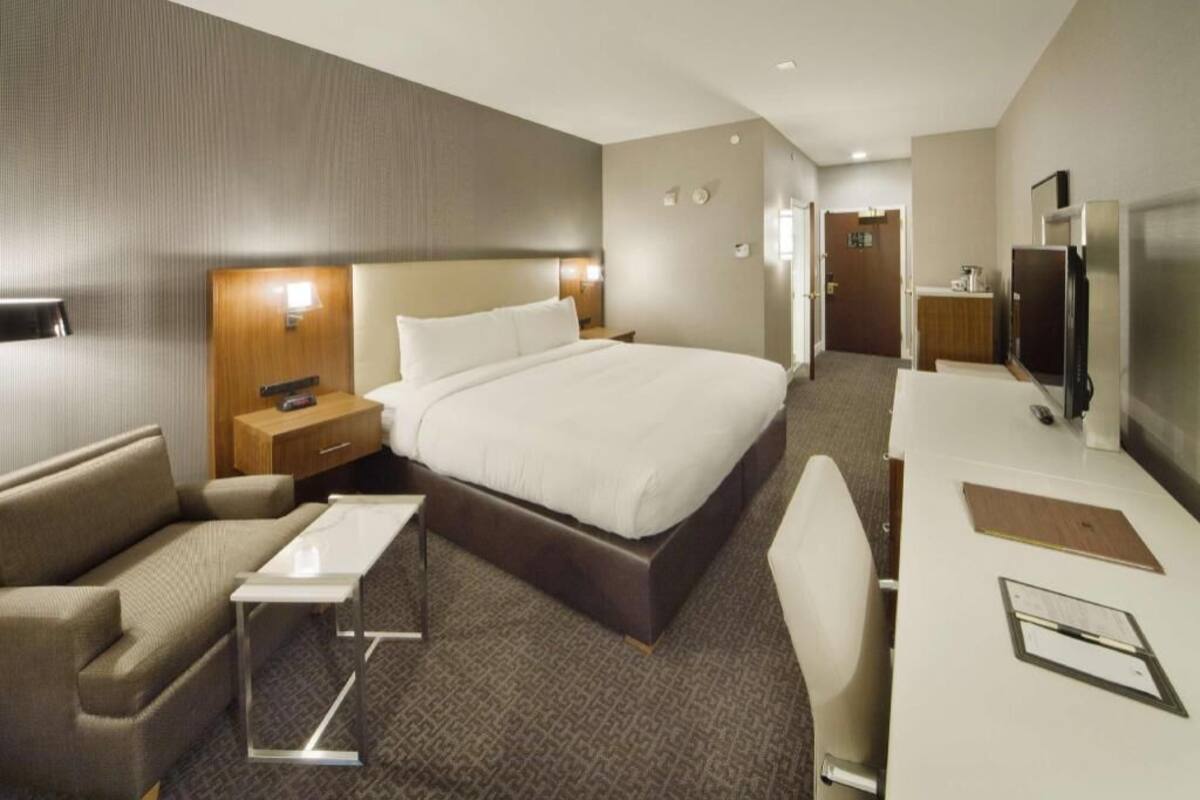 A hotel room with a large bed, a desk with a chair, a sofa, a bedside table, and a TV.