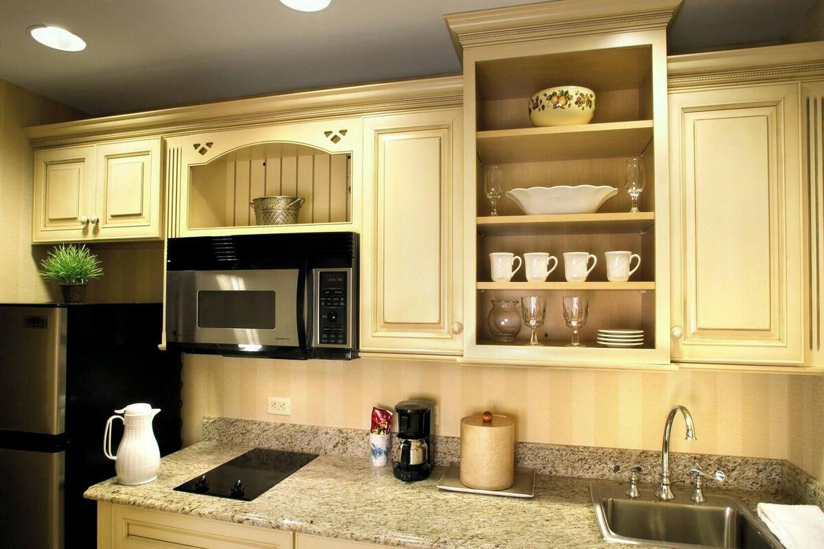 A kitchen with a built-in microwave, a coffee maker, a sink, and a cabinet with dishes and glasses.