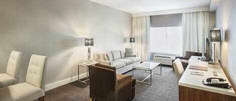 Una habitación de hotel con un sofá, dos sillones, un escritorio y una mesita.
