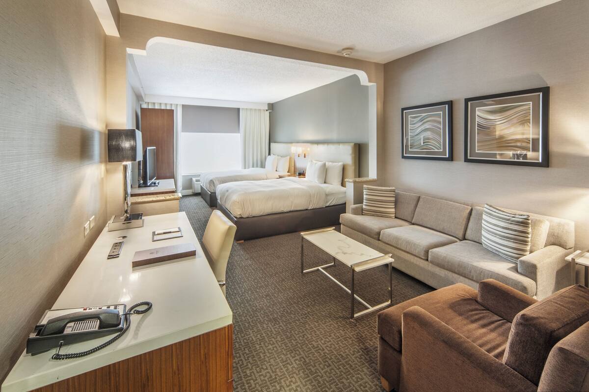 A hotel room with a bed, a sofa, a desk, and a TV.
