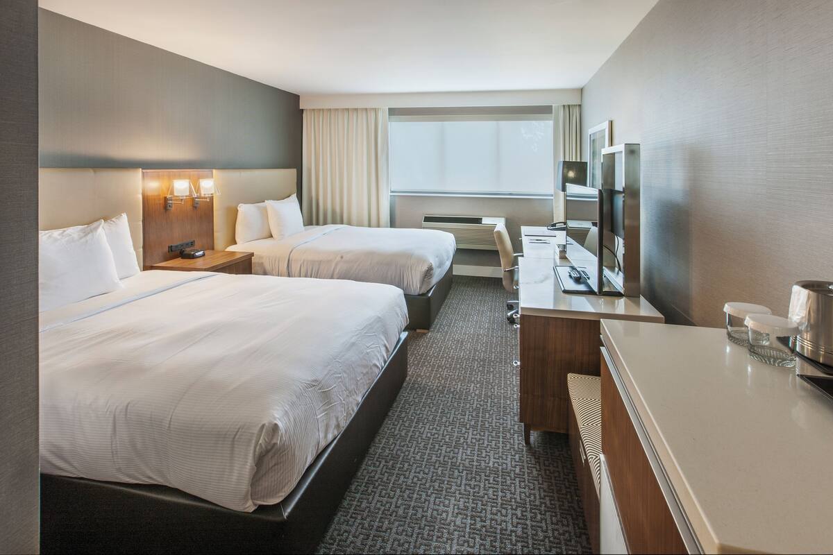 A hotel room with two beds, a desk, a TV, and a window with curtains.
