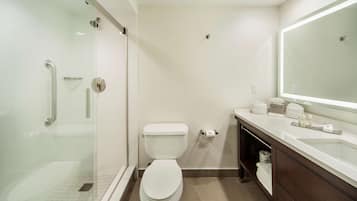 A modern bathroom with a glass shower enclosure, a white toilet, a sink with a mirror, and a dark wooden vanity.