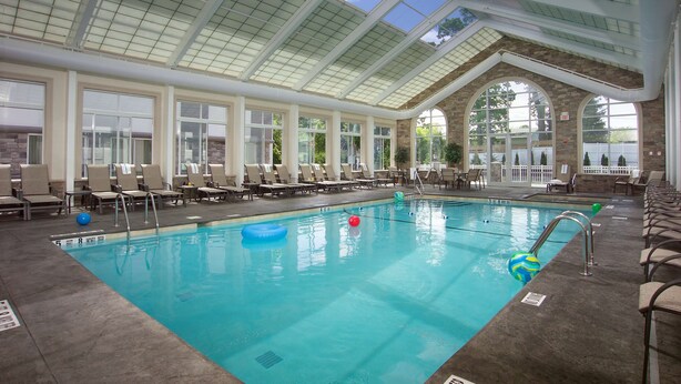An indoor swimming pool with clear glass ceilings, stone walls, and multiple lounge chairs around the pool area. - DoubleTree by Hilton Hotel Nanuet (Nanuet)