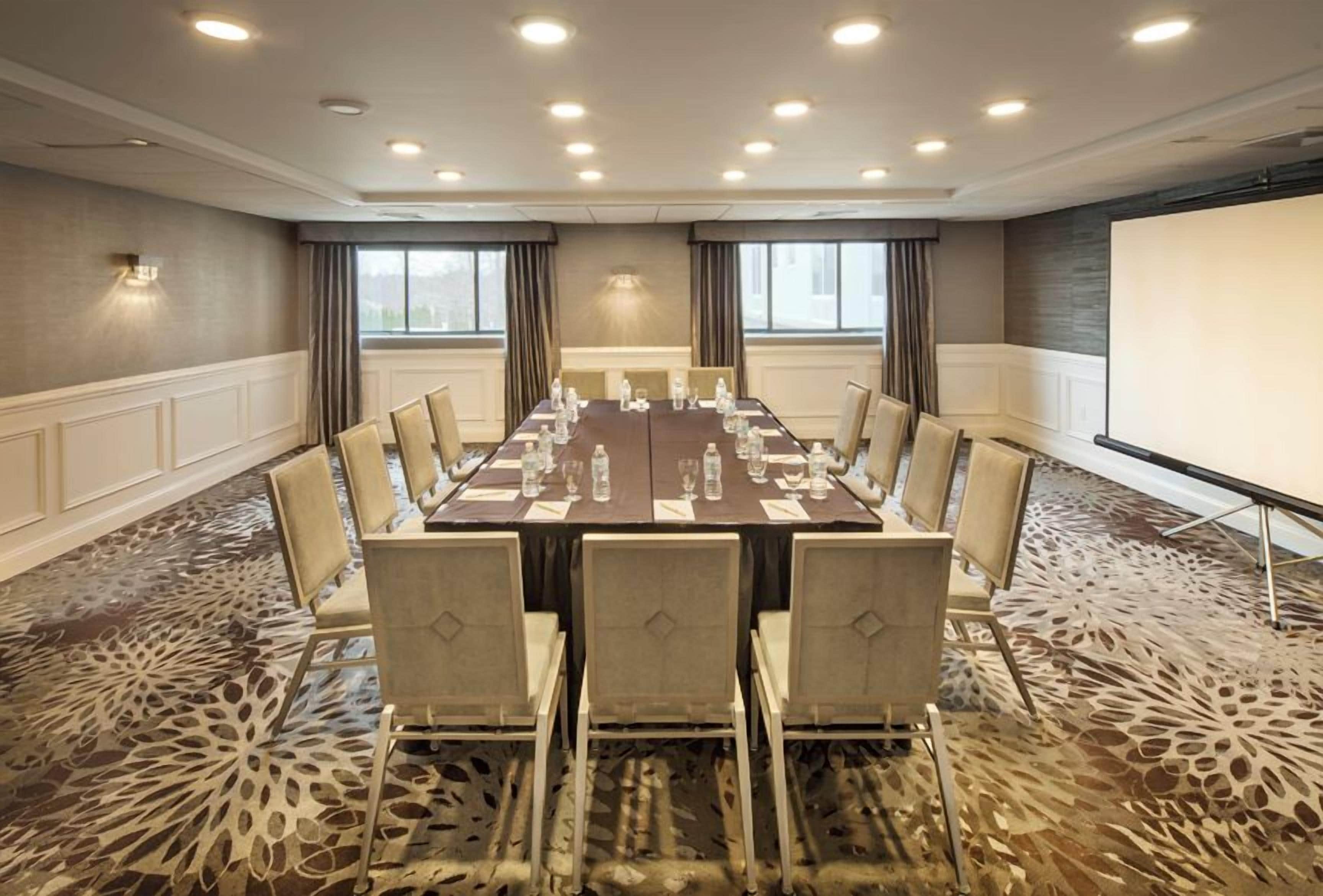 A conference room with a long table, chairs, a projector screen, and a carpeted floor.