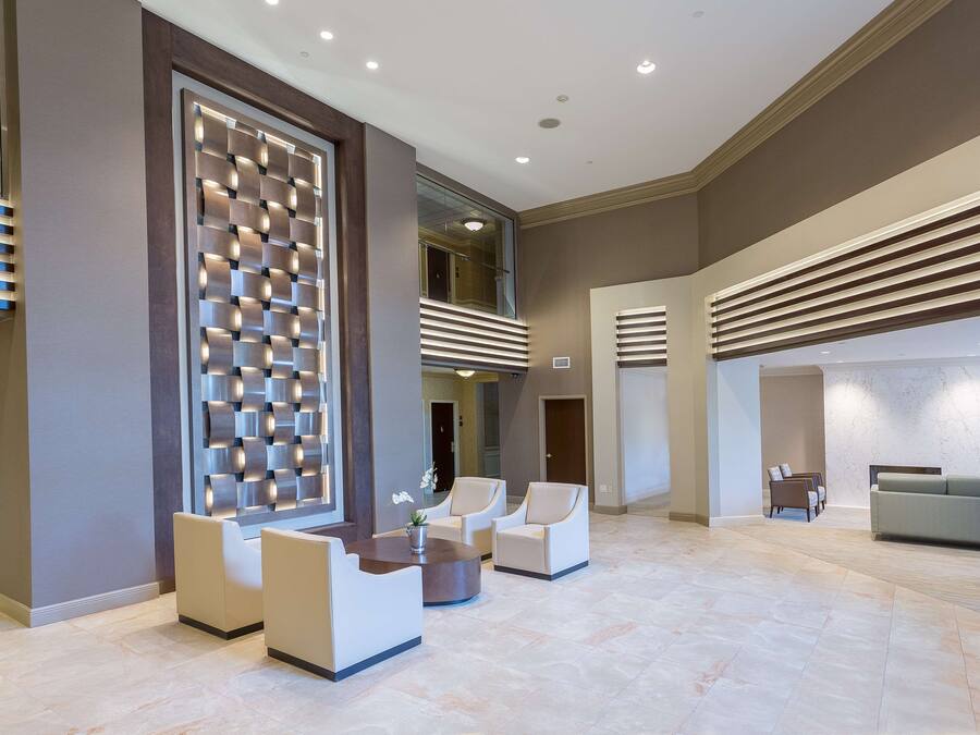 A spacious lobby with a modern design, featuring a seating area with sofas and armchairs, a decorative wall panel, and a large window providing natural light.