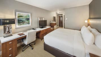 Habitación de hotel con cama, escritorio, silla, televisor y un cuadro en la pared.