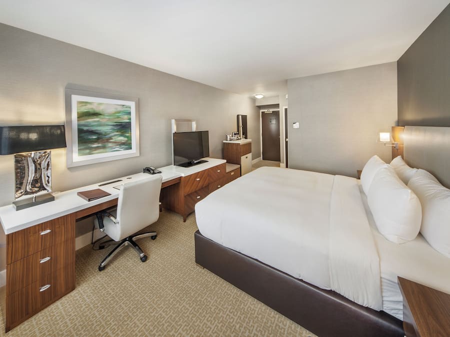 Habitación de hotel con cama, escritorio, silla, televisor y un cuadro en la pared.
