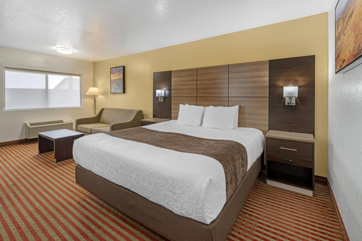 Ein Hotelzimmer mit einem großen Bett, einer Couch, einem Nachttisch, einer Lampe und einem an der Wand befestigten Fernseher.