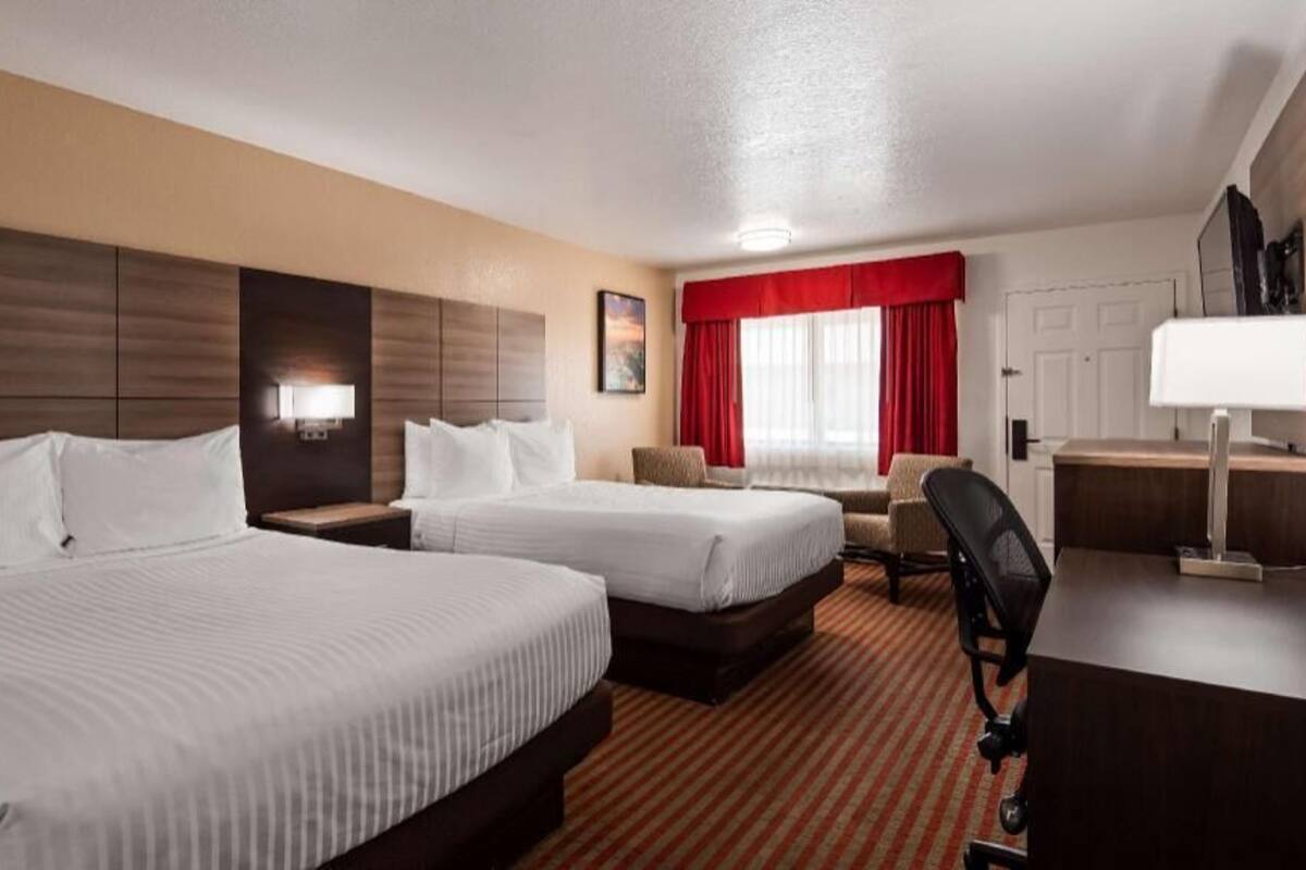 Ein Hotelzimmer mit zwei Betten, einem Schreibtisch, einem Stuhl, einem Fernseher und einem Fenster mit roten Vorhängen.