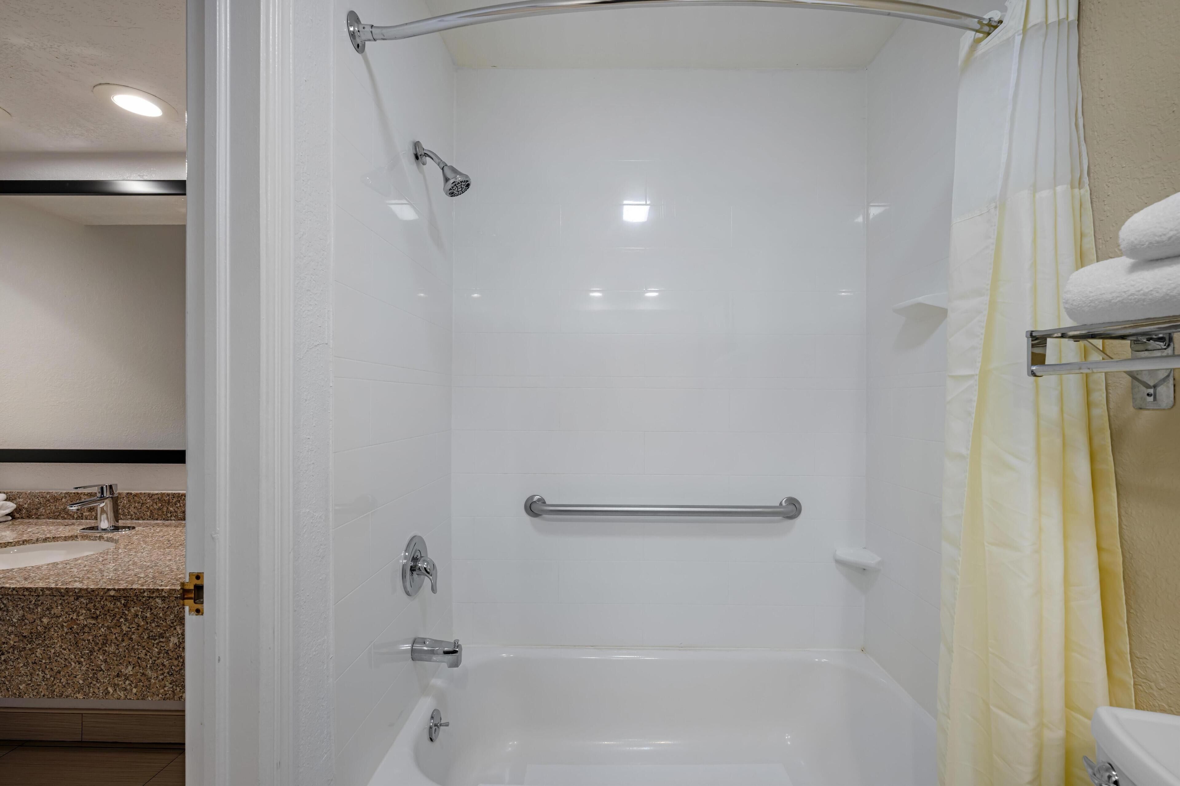 Un baño moderno con ducha a nivel, barra de apoyo y inodoro con toallero.
