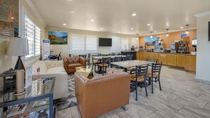 A spacious dining area with multiple tables and chairs, a kitchen area with wooden cabinets, and a comfortable seating area with a sofa and chairs.