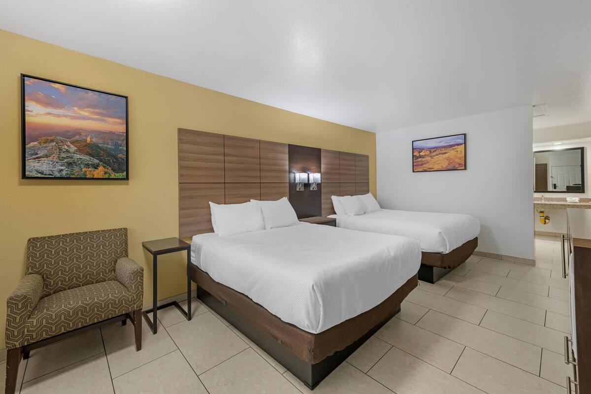 Ein Hotelzimmer mit zwei Betten, einem Sessel, einem kleinen Tisch und zwei Bildern an den Wänden.