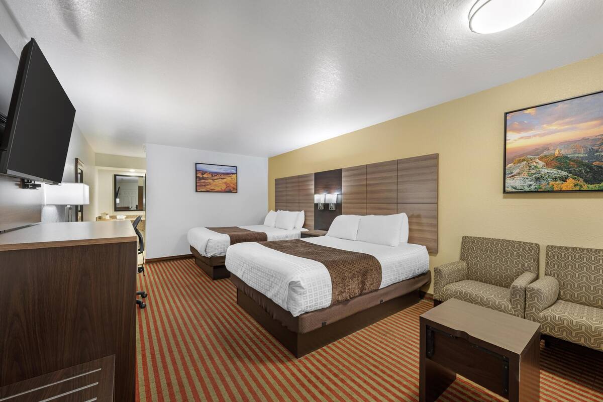 Ein Hotelzimmer mit zwei Betten, einem Schreibtisch, einem Fernseher und einem Sofa.