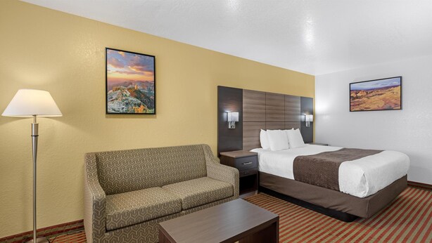 A hotel room with a sofa, a bed, a nightstand, a lamp, and two paintings on the walls.