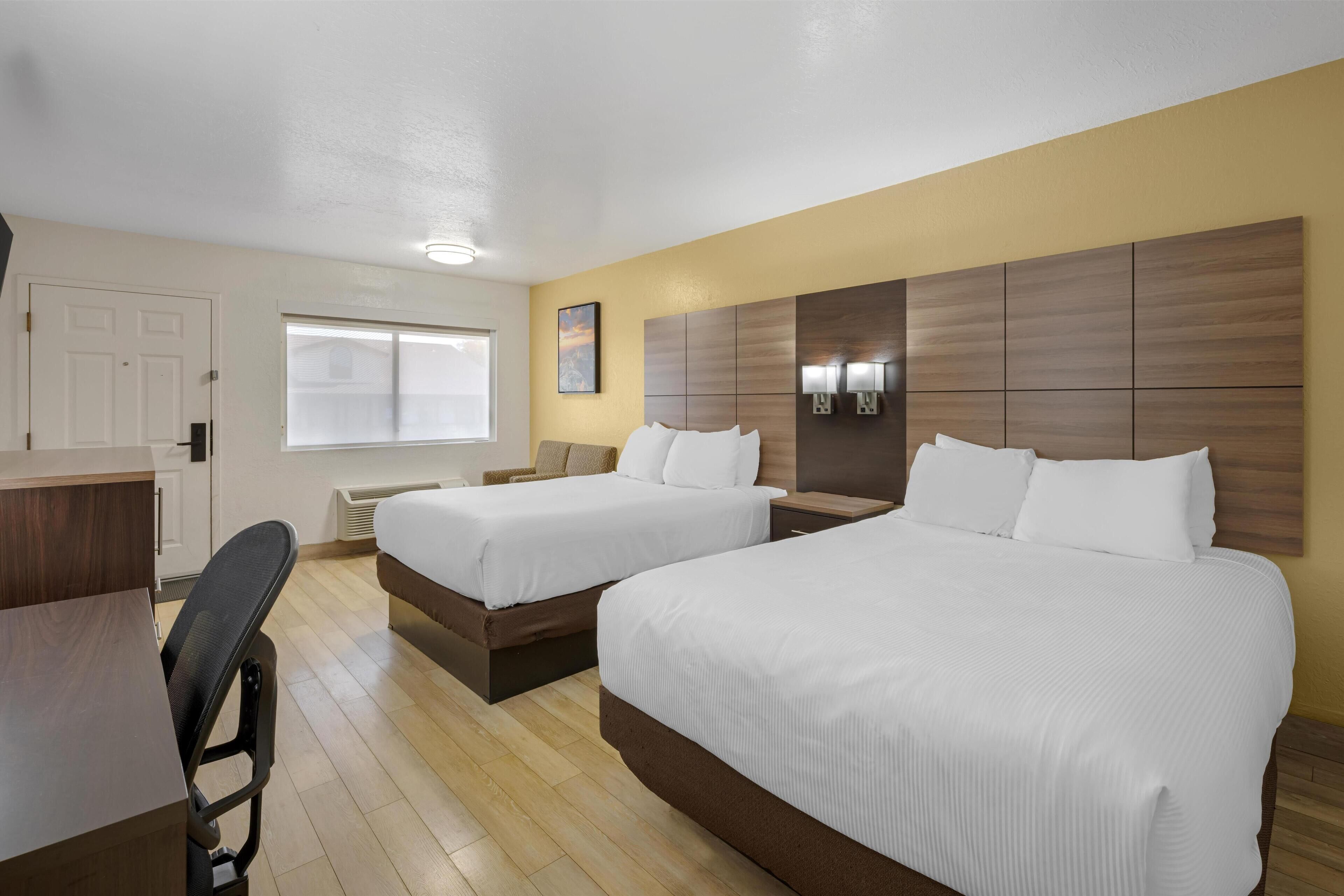 A hotel room with two beds, a desk, and a chair.